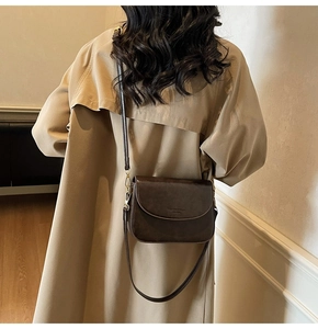 Detail view of a vintage dark brown leather crossbody bag styled with a khaki trench coat