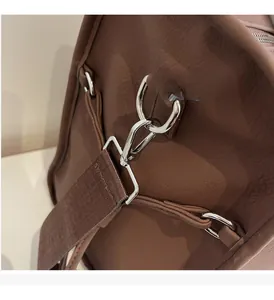 Close-up of silver metal swivel hook and textured fabric strap on brown leather bag