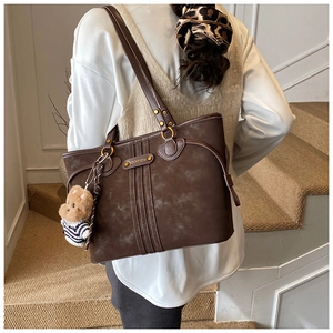 Detail of dark brown tote bag with vertical stitching and cute teddy bear charm accessory