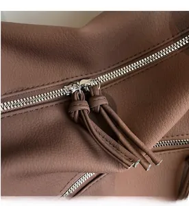 Detail view of smooth silver zipper with knotted brown leather pullers on stylish travel bag