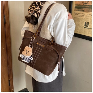 Detailed side view of deep brown vintage tote bag with metal tag and cute bear charm