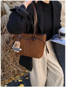 Detail of a brown suede tote bag featuring a cute teddy bear charm and metal brand plate