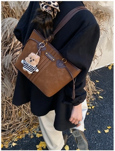 Brown suede tote bag with leather straps and cute plush bear charm in autumn setting