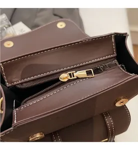 Detail of smooth gold metal zipper and white contrast stitching on dark brown leather bag