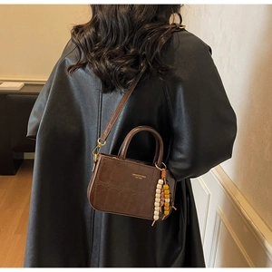 Detalle de bolso marrón oscuro con efecto cocodrilo y cuentas sobre abrigo de piel negra
