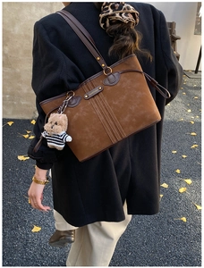 Detail of brown suede tote bag with brand logo and cute bear pendant on autumn street
