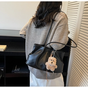 Détail d'un sac cabas noir plissé avec un joli porte-clé en peluche d'ours brun sur le côté