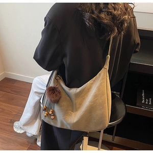 Detail of grey suede shoulder bag with plush ball charm on model in a modern room
