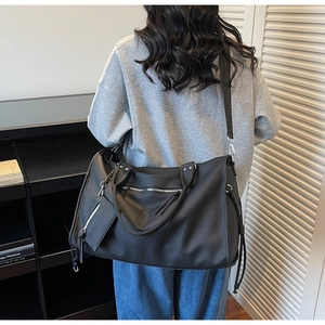 Close-up of a black matte leather tote bag with silver zippers and adjustable shoulder strap