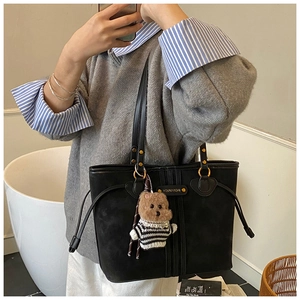 Close-up of black suede tote bag with metal logo and cute striped teddy bear pendant