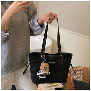 Detail of black tote bag featuring a vintage badge and cute striped puppy plush charm