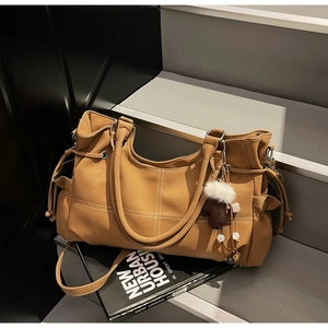 Dettaglio borsa tote marrone con cuciture bianche e ciondolo a cuore in peluche