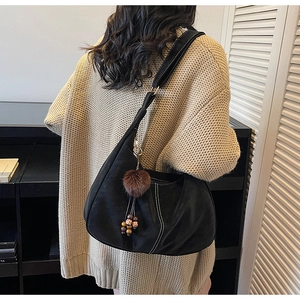 Detail of black matte leather hobo bag with vintage plush ball and wooden bead charm