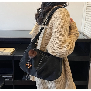 Detail of black large capacity shoulder bag with white contrast stitching and faux fur charm