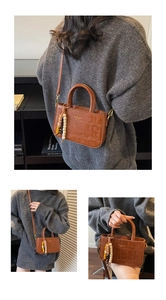 Detalle del bolso marrón con textura de cocodrilo, colgante de cuentas y asa redondeada