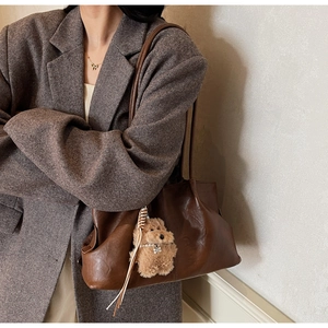Gros plan du sac cabas en cuir marron vintage avec porte-clés chien en peluche et blazer