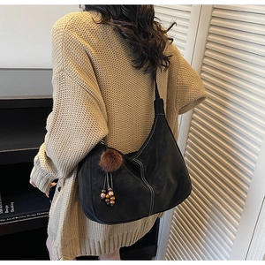 Detail of black suede hobo bag with contrast stitching and plush charm on model