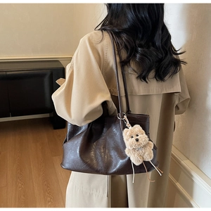 Détail d'un sac cabas en cuir marron foncé avec texture souple et porte-clé peluche