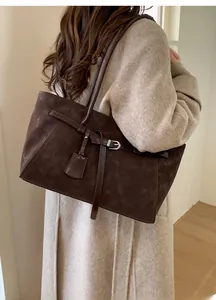Detail of a large dark brown suede tote bag featuring leather straps and side hanging tags