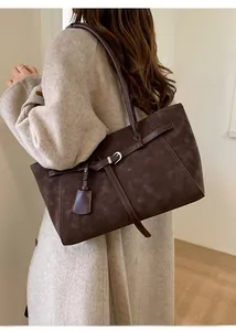 Detail of dark brown suede tote bag with metal buckle and slim shoulder strap shown on model