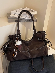 Borsa tote marrone scuro con cuciture a contrasto e ciondolo a guanto su sfondo di libri