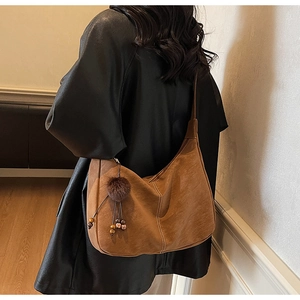 Brown suede hobo shoulder bag with decorative fur ball and wooden bead charms on model