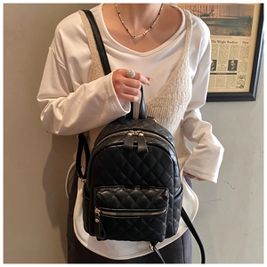 Detail shot of a black quilted mini backpack with gold zippers worn by a model