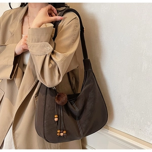 Detail of dark coffee leather shoulder bag with plush ball charm and bead tassel