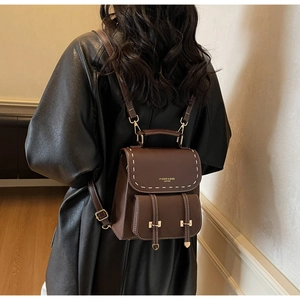 Detail of dark brown leather backpack featuring contrast white stitching and gold hardware