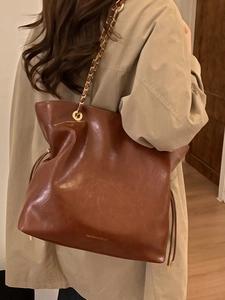 Sac cabas marron en cuir avec cordon de serrage et chaîne dorée porté à l'épaule