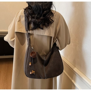 Detail of vintage brown suede shoulder bag with contrast stitching and pom-pom charm