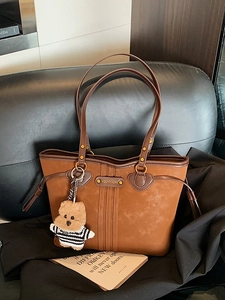 Brown vintage suede tote bag with heart details and a cute bear charm on a black sofa