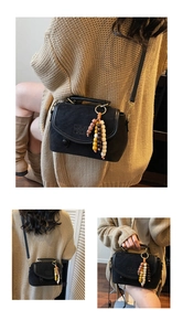 Detail of black suede crossbody bag featuring embossed lettering and colorful bead charm