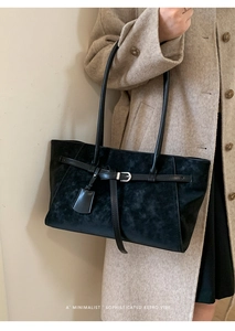 Detail of minimalist black suede tote bag featuring slim straps and metal buckle accents