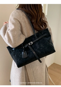 Detail of a large black matte leather tote bag worn over a beige wool coat
