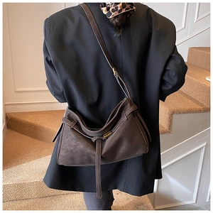 Détail d'un sac cabas en daim marron foncé avec boucle métallique porté à l'épaule