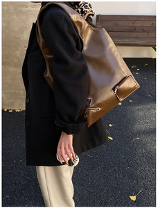 Detail of a large brown faux leather tote bag with exterior zipper and drawstring accents