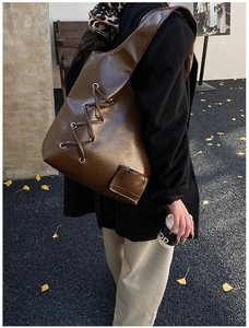 Detail of a dark brown glossy leather tote bag with stylish cross-laced straps
