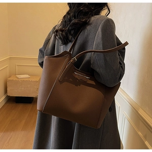 Detail view of the deep brown litchi grain leather tote bag worn as an underarm shoulder bag