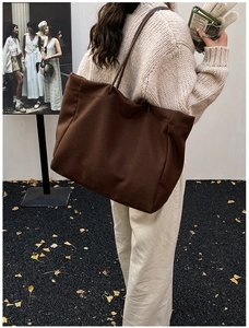 Close-up of a large brown felt tote bag worn over the shoulder in a minimalist fall setting