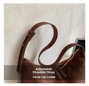 Close-up of adjustable shoulder strap and gold zipper on brown suede underarm bag