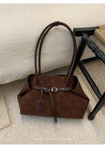 Detail of dark brown suede tote bag with leather buckle and metallic hardware on rug