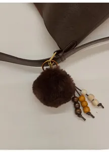 Détail d'un sac seau en cuir marron foncé avec un pompon en fausse fourrure et des perles
