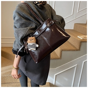 Dettaglio di grande borsa tote marrone scuro con cuciture verticali e ciondolo a forma di orso