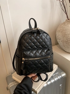 Minimalist black quilted mini backpack with gold hardware on luggage background