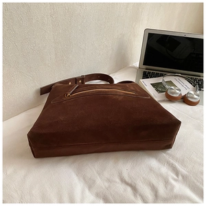 Detailed macro view of dark brown suede tote bag featuring a decorative metal zipper pocket