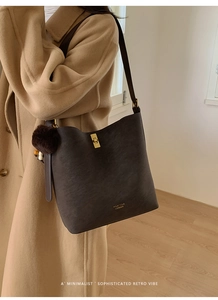 Détail du sac seau marron foncé en daim avec fermoir doré et pendentif pompon doux