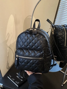Minimalist black quilted backpack with gold hardware shown on a stylish desk setup