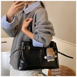 Dettaglio borsa tote nera lucida plissettata con cinturino in pelle e ciondolo a orso