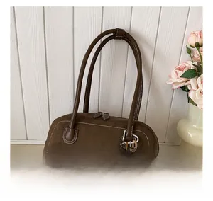 Detail of dark brown suede shoulder bag with contrast stitching and bear charm